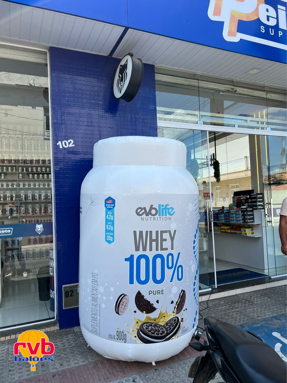 Pote de Whey Gigante em frente a loja de suplementos